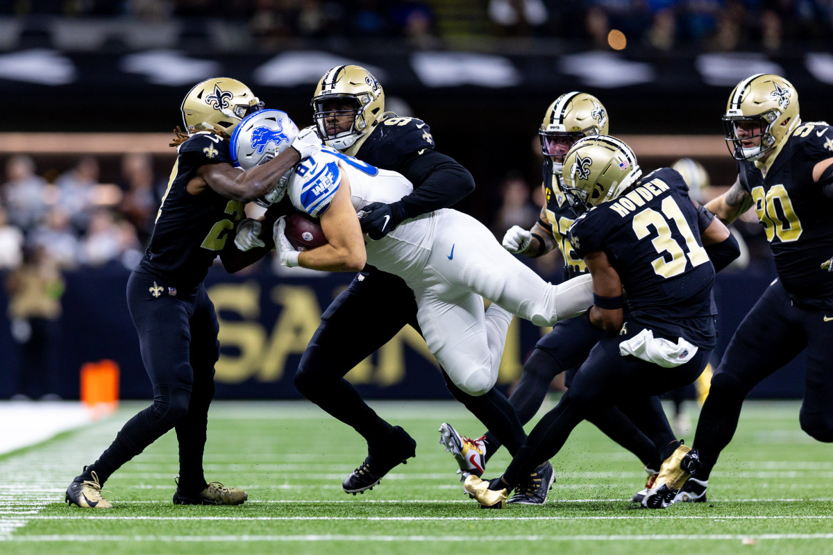 Sam LaPorta holds the ball as he is. tackled in the air by a bunch of Saints players